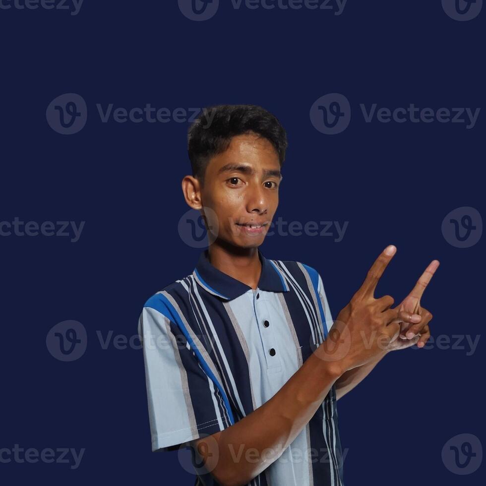 excited asian man wearing colorful t-shirt pointing to the copy space on the side, isolated blue background. photo