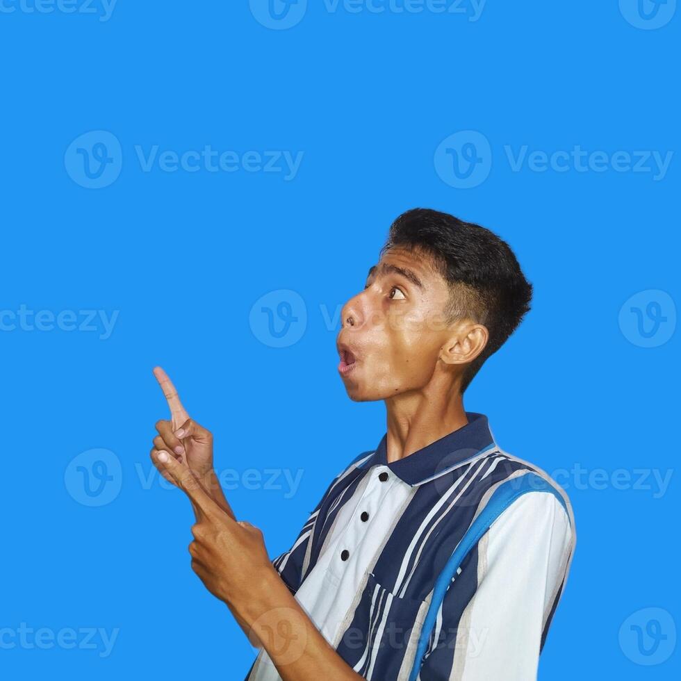 excited asian man wearing colorful t-shirt pointing to the copy space on the side, isolated blue background. photo