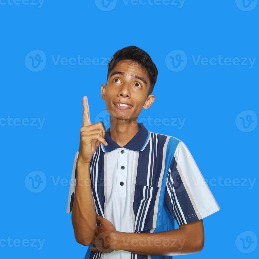 Outward looking young Asian man wearing colorful t-shirt, copy space index finger with new idea, isolated on blue background photo