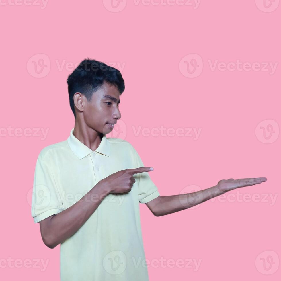 Excited Asian man wearing yellow t-shirt pointing at copy space on the side, isolated on pink background photo