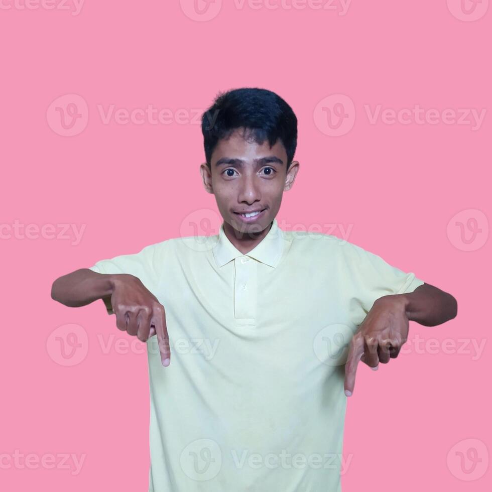 excited asian man wearing yellow t-shirt pointing to the copy space on the side, isolated blue background. photo