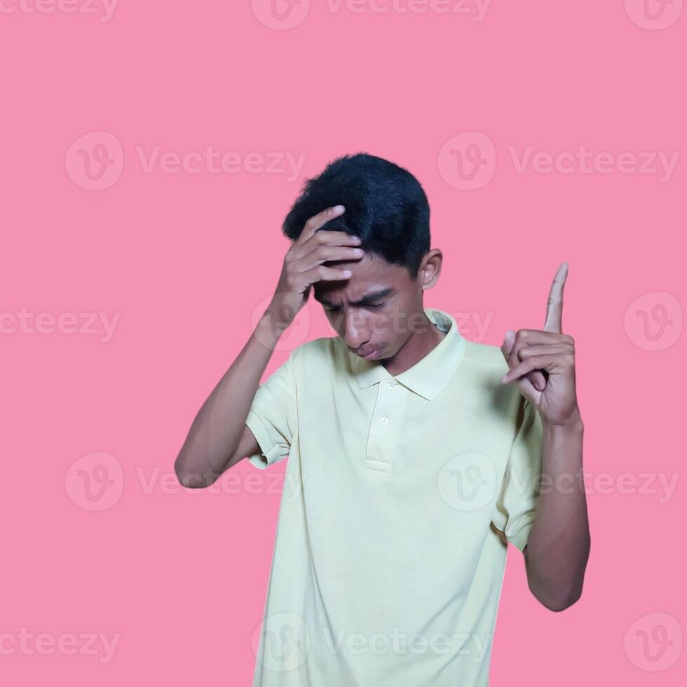 Dizzy face holding head of young Asian man in yellow shirt isolated on pink background photo