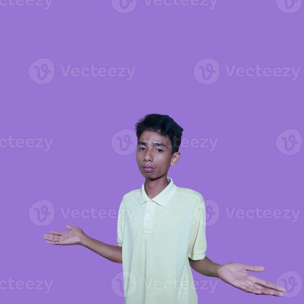 young asian man with a surprised face facing the camera, with both hands to the side, wearing a yellow blue t-shirt, isolated on a purple background photo