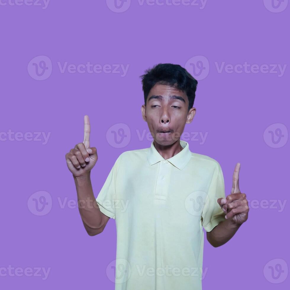 excited asian man wearing yellow t-shirt pointing to the copy space on the side, isolated purple background. photo