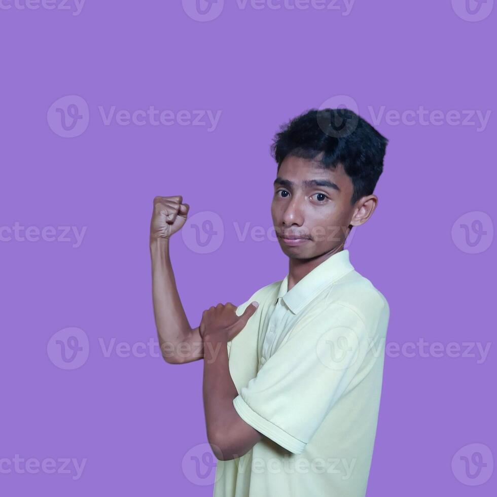 Excited Asian man wearing yellow t-shirt showing strong movement raising arms purple background. photo