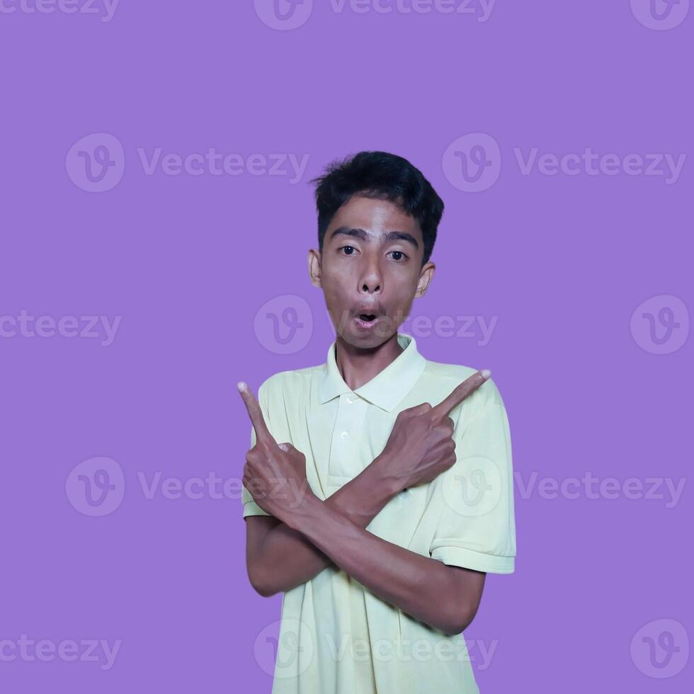 excited asian man wearing yellow t-shirt pointing to the copy space on the side, isolated pink background. photo