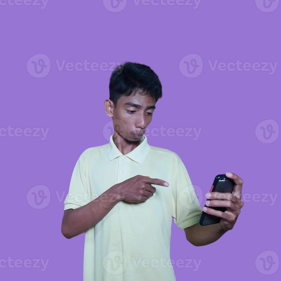 excited asian man wearing yellow t-shirt pointing to the copy space on the side, isolated pink background. photo