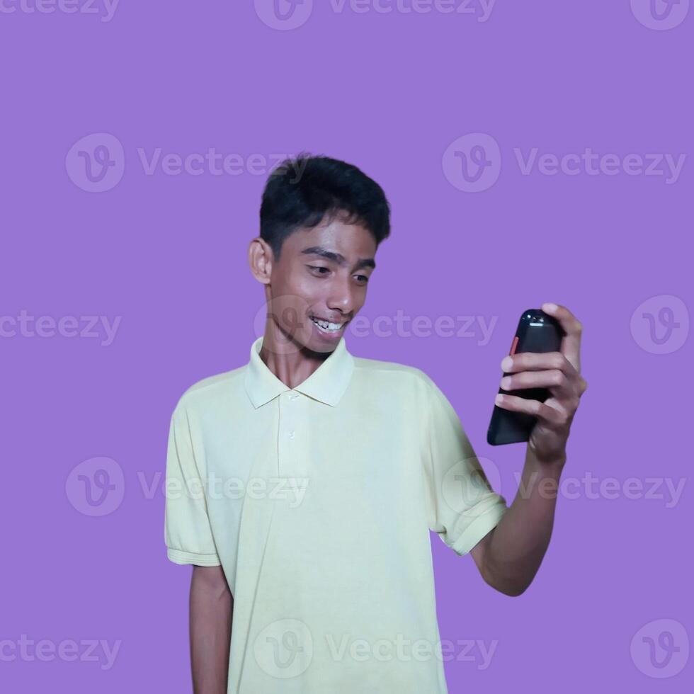 Young asian man surprised looking at smart phone, wearing yellow t-shirt, isolated pink background. photo