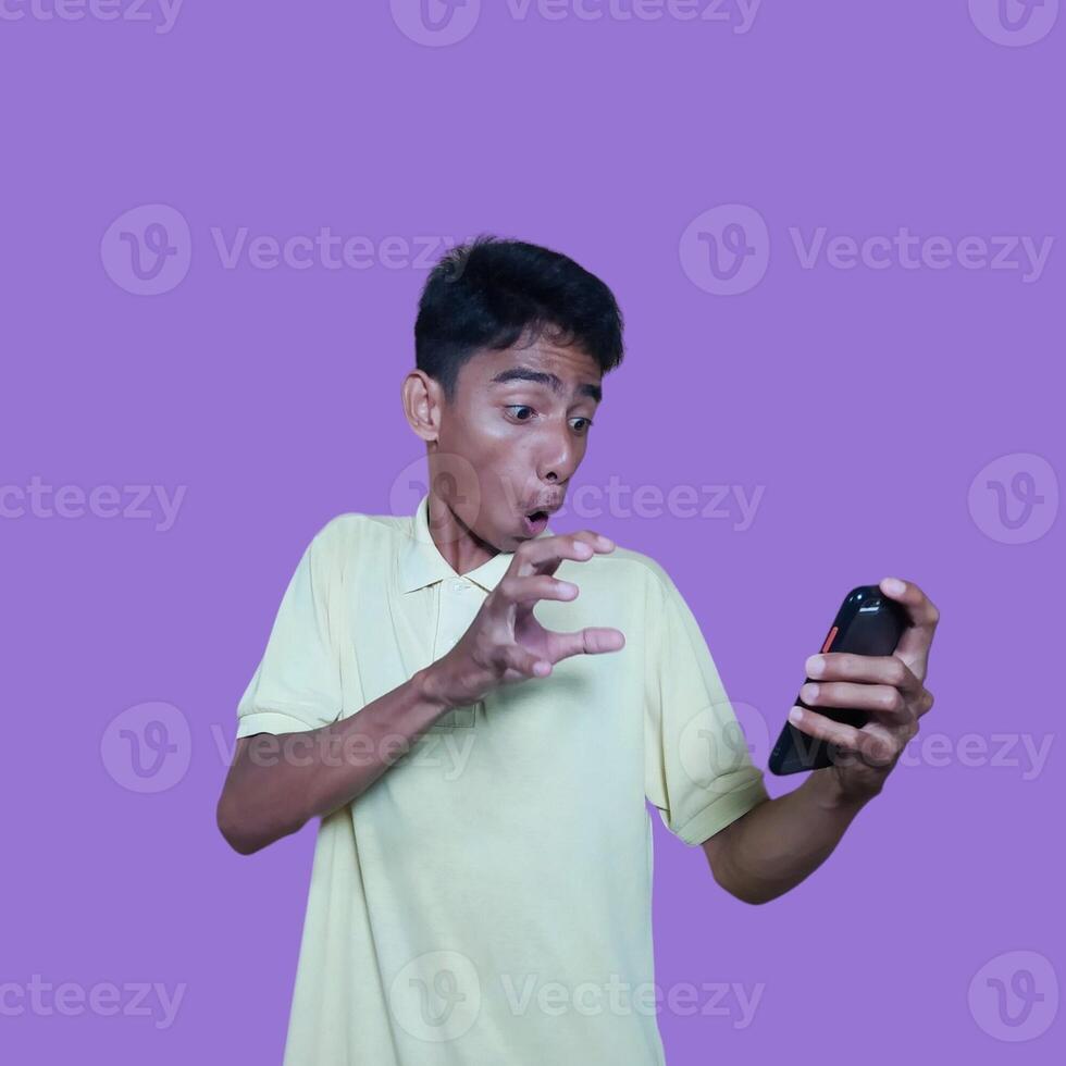 Young asian man surprised looking at smart phone, wearing yellow t-shirt, isolated pink background. photo