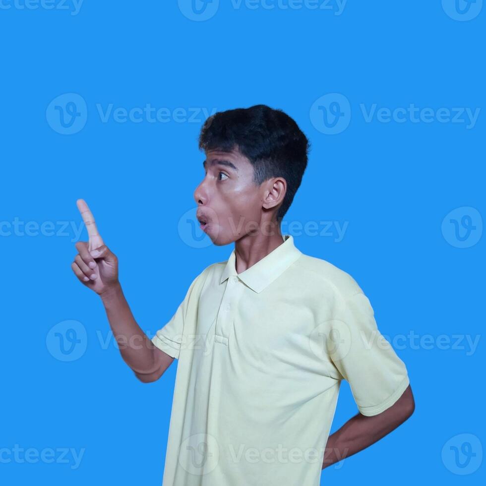 excited asian man wearing yellow t-shirt pointing to the copy space on the side, isolated blue background. photo