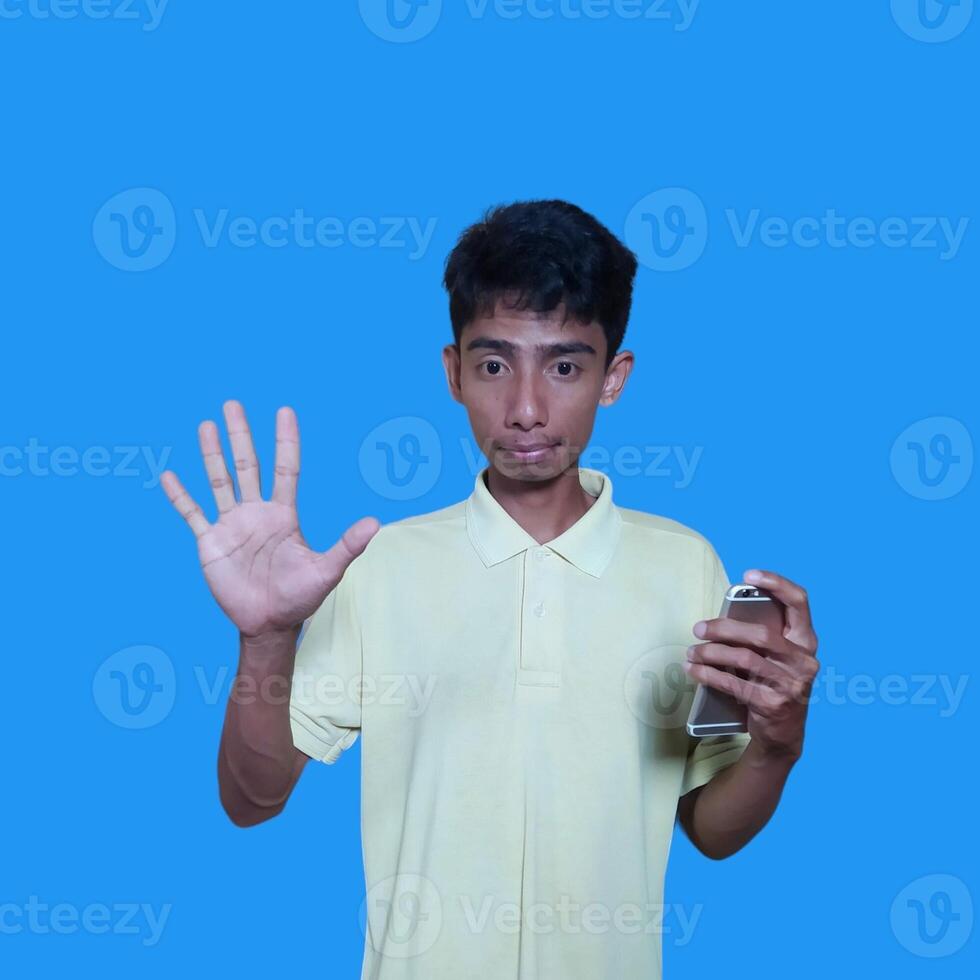 Excited Asian man wearing yellow t-shirt giving number 12345 hand gesture. blue background photo