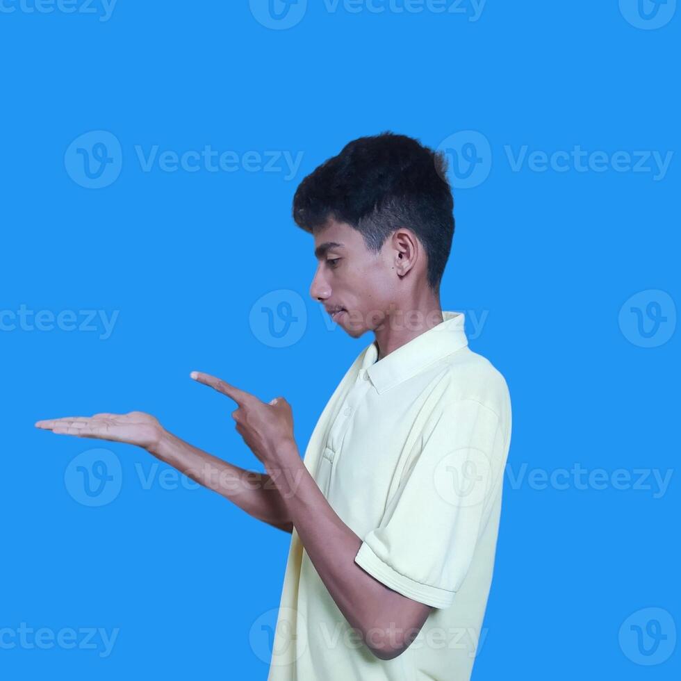 Excited Asian man wearing yellow t-shirt pointing at copy space on the side, isolated on purple background. photo