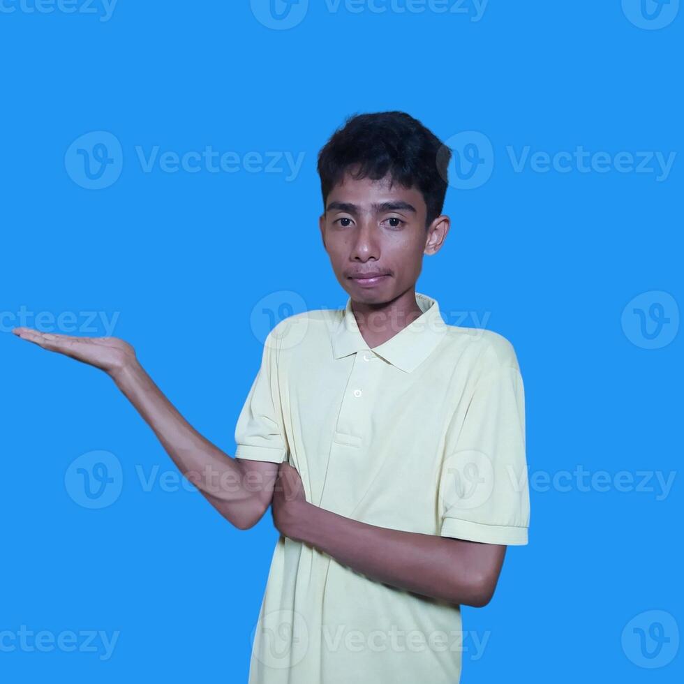 Excited Asian man wearing yellow t-shirt pointing at copy space on the side, isolated on purple background. photo