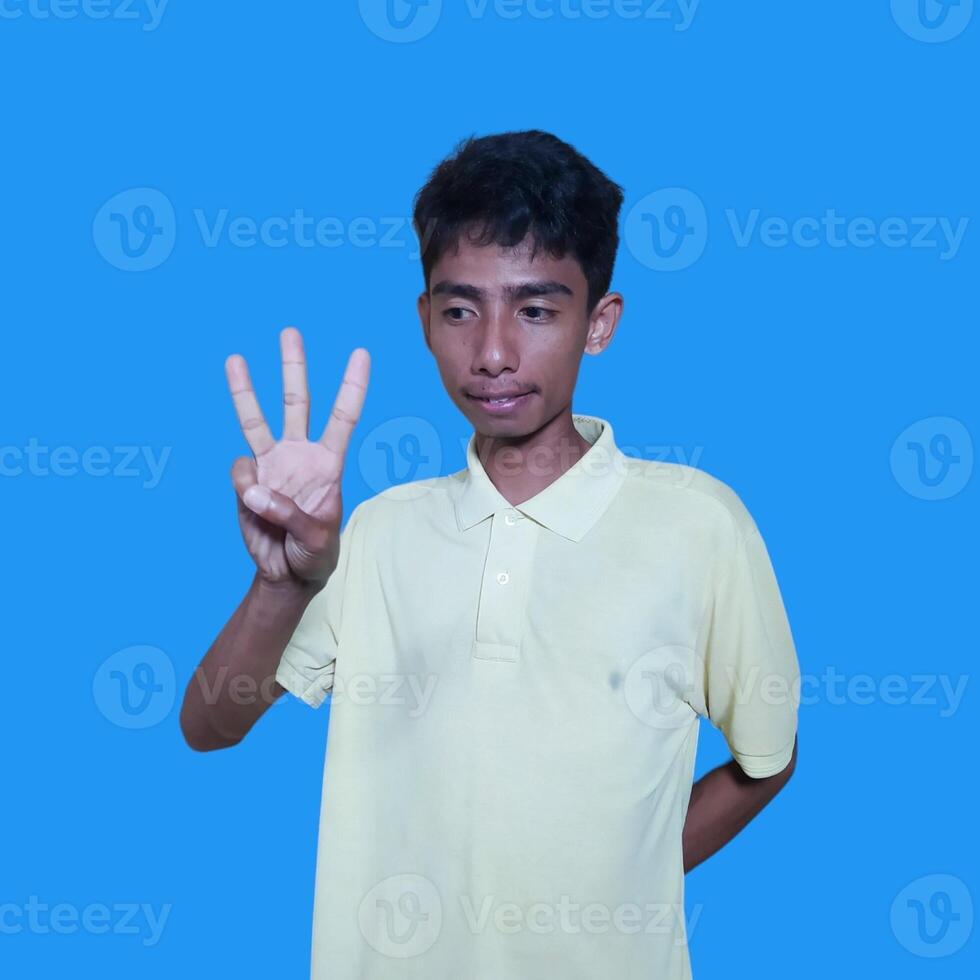 Excited Asian man wearing yellow t-shirt giving number 12345 hand gesture. blue background photo