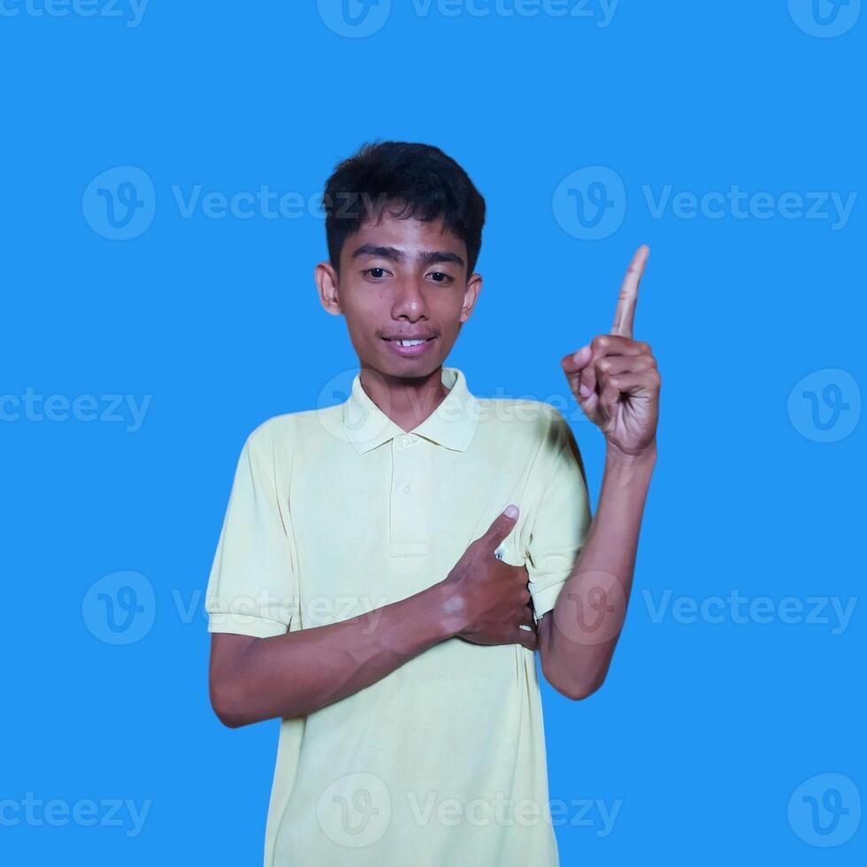 excited asian man wearing yellow t-shirt pointing to the copy space on the side blue background. photo