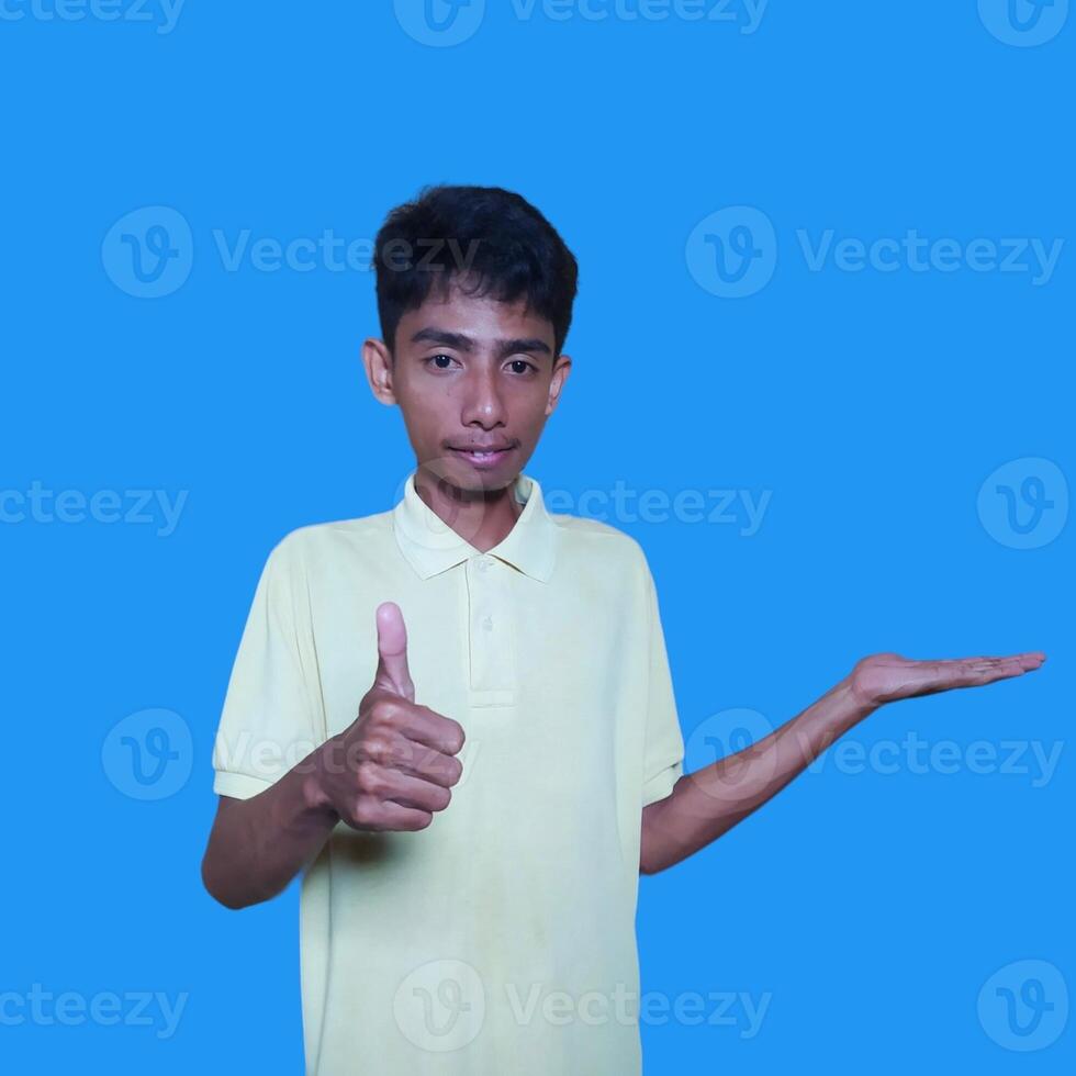 Excited Asian man wearing yellow t-shirt pointing at copy space on the side, isolated on purple background. photo