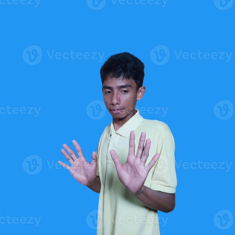 young asian man hands stop. with a serious face wearing a yellow t-shirt, isolated on a blue background photo