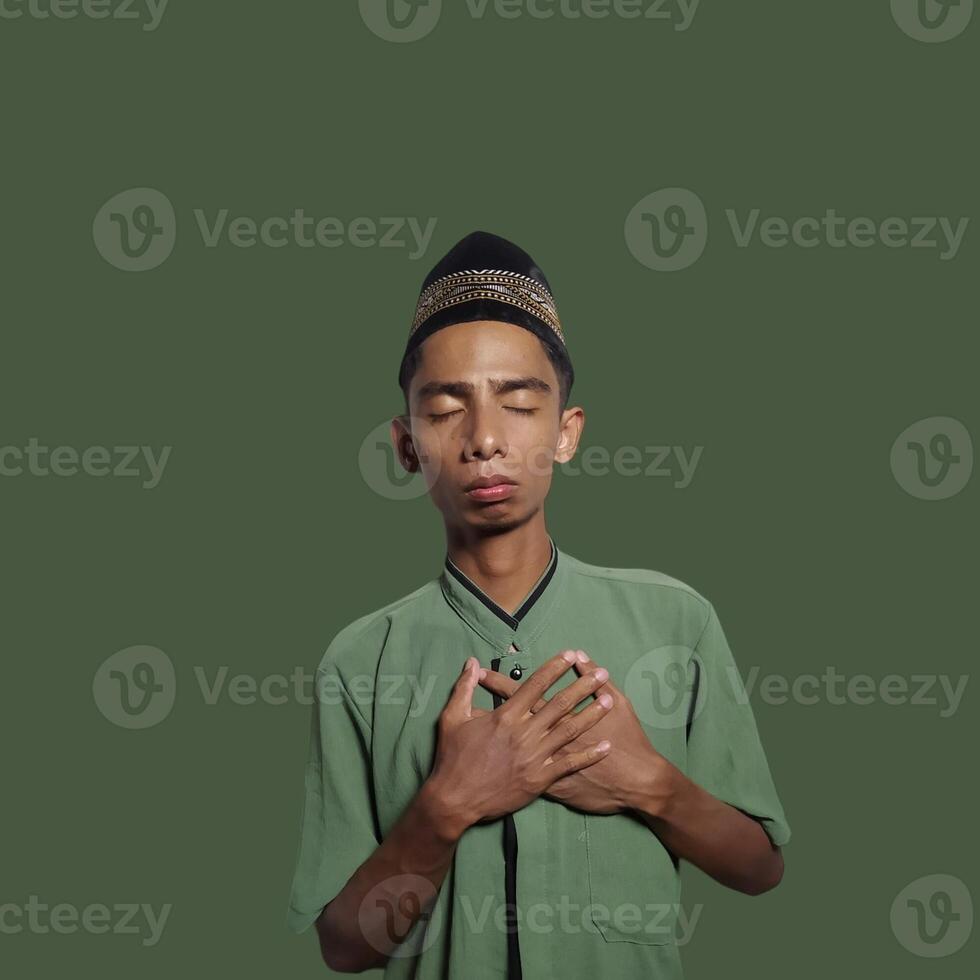 Young Asian man praying wearing green muslim clothes during ramadan green background photo