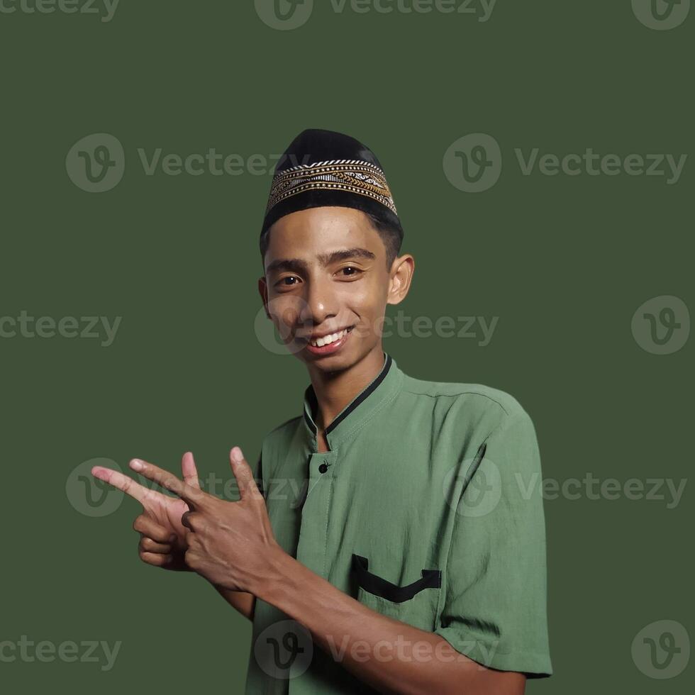 excited asian man wearing ramadan muslim clothes. pointing to copy space with side blue background. photo