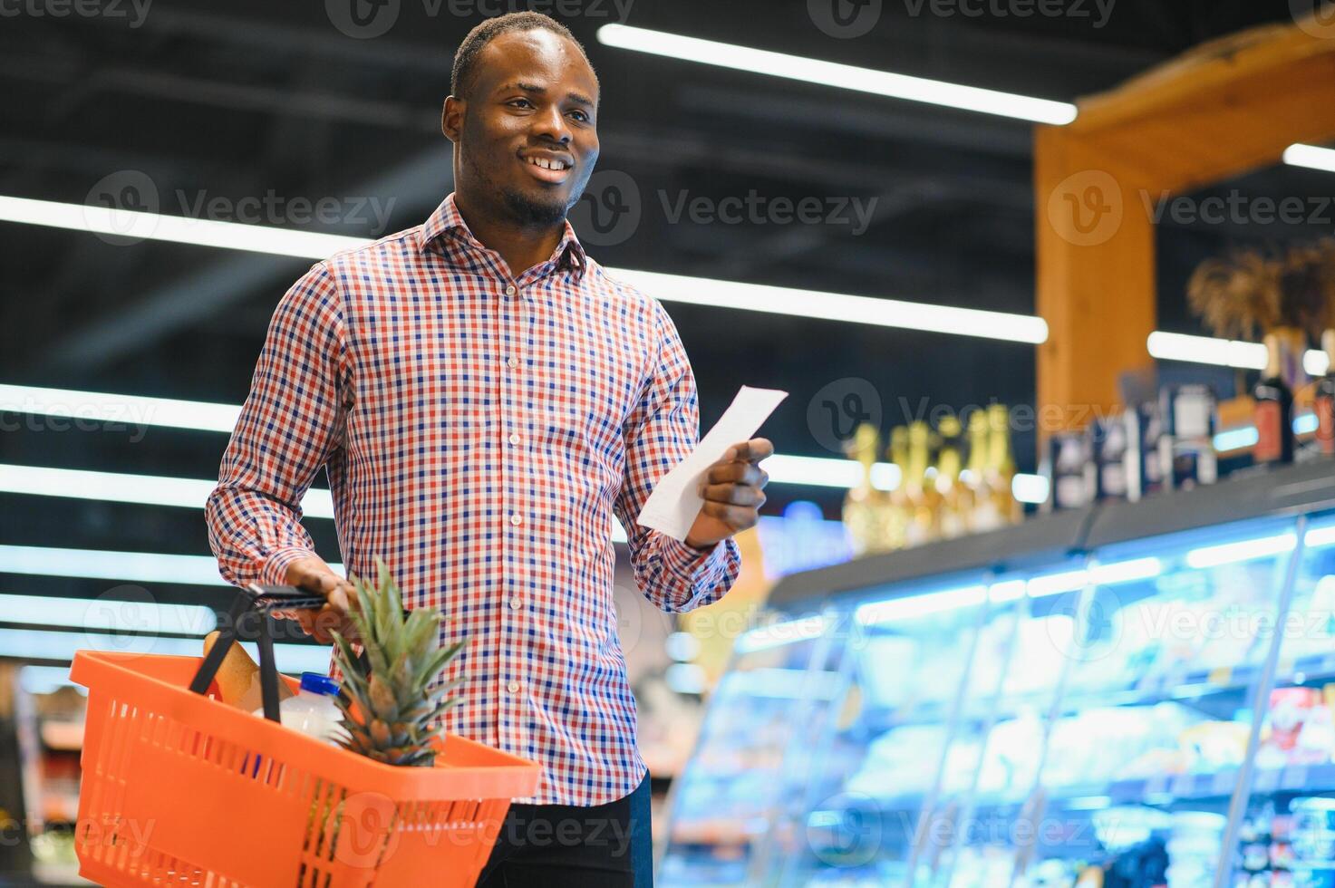 Surprised African-American man looks at receipt total in sales check holding paper bag photo