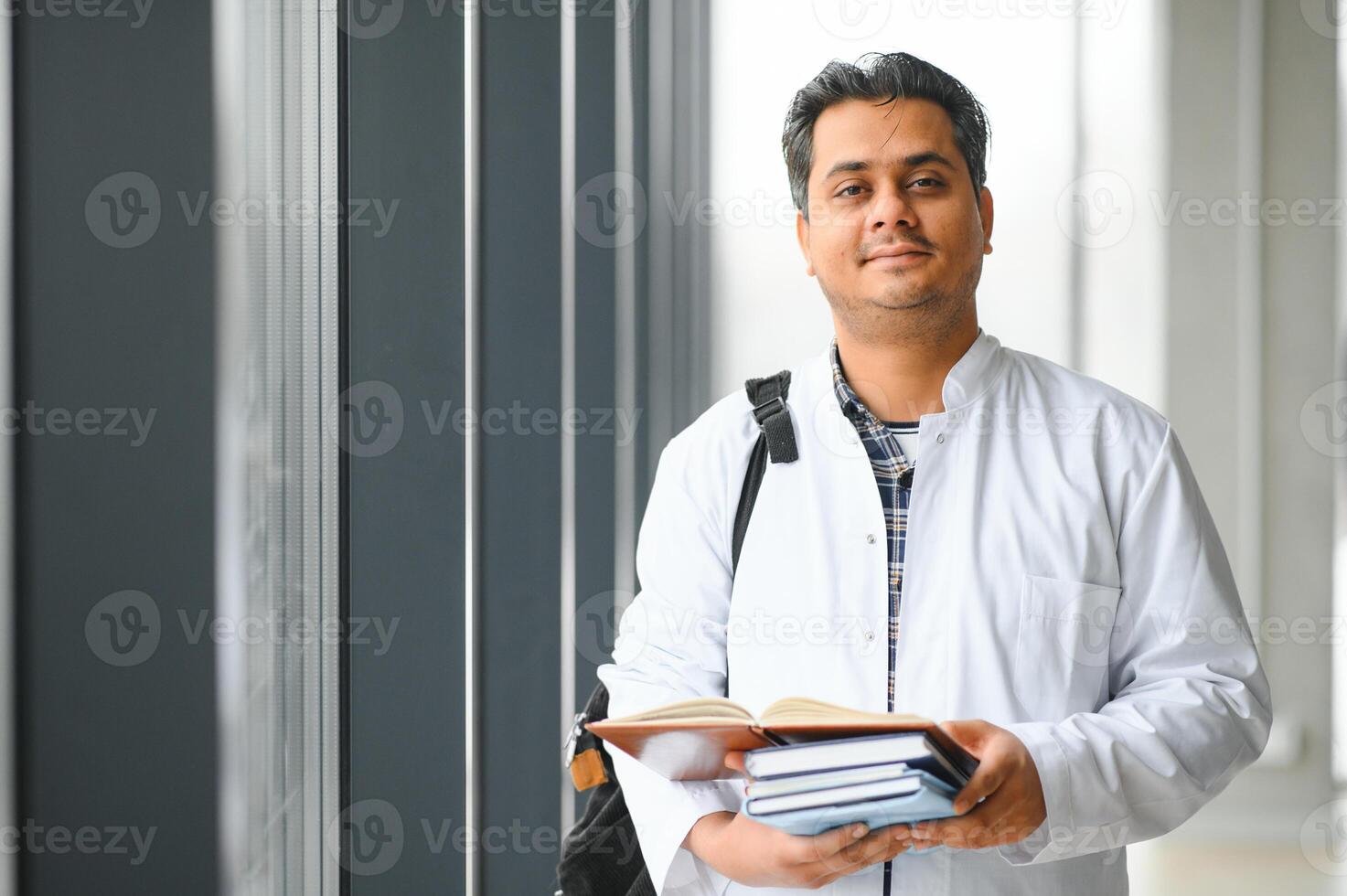 Portrait of a young Indian male medical student in a white coat waving photo