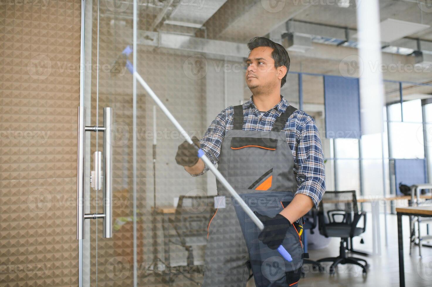 Male professional cleaning service worker in overalls cleans the windows and shop windows photo