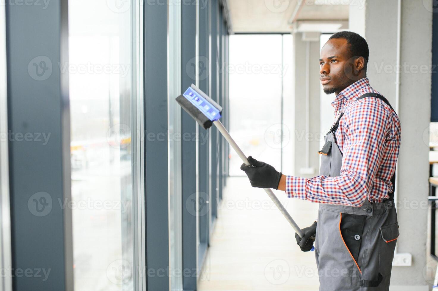 African Male professional cleaning service worker in overalls cleans the windows and shop windows of a store with special equipment photo