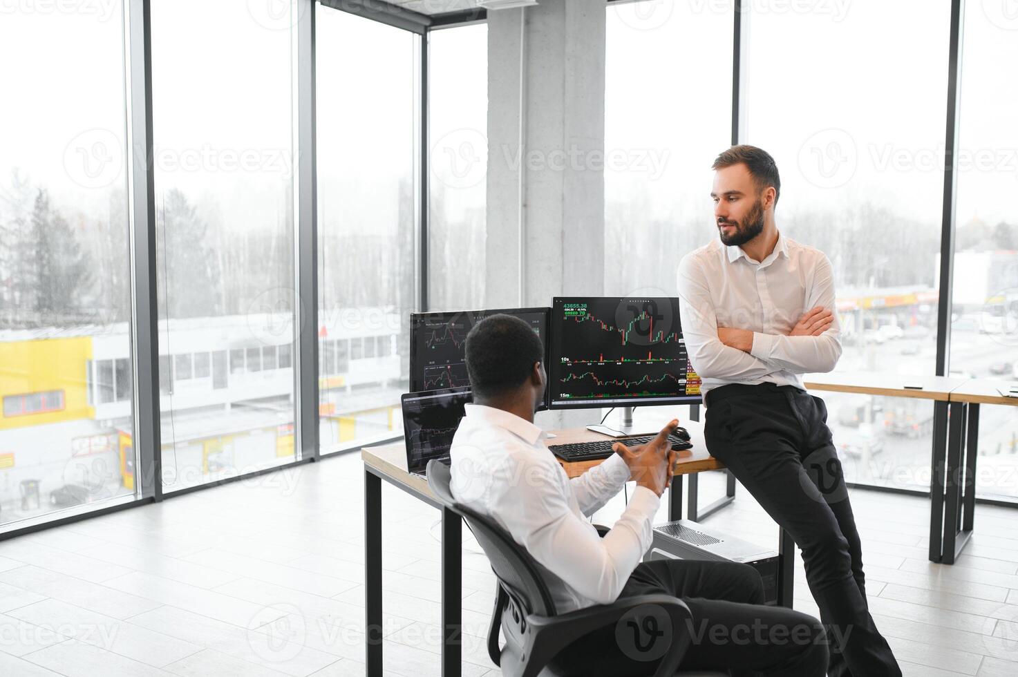 Two successful trader sitting in office, checking cryptocurrency information data on finance market graph, pointing on monitor photo