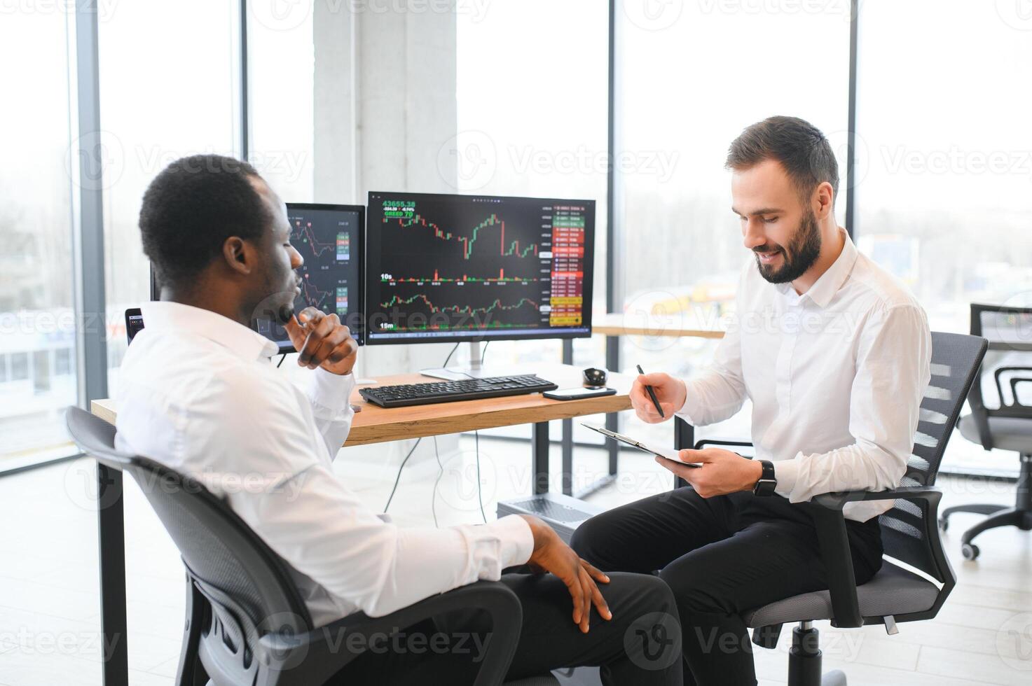 Two successful trader sitting in office, checking cryptocurrency information data on finance market graph, pointing on monitor photo