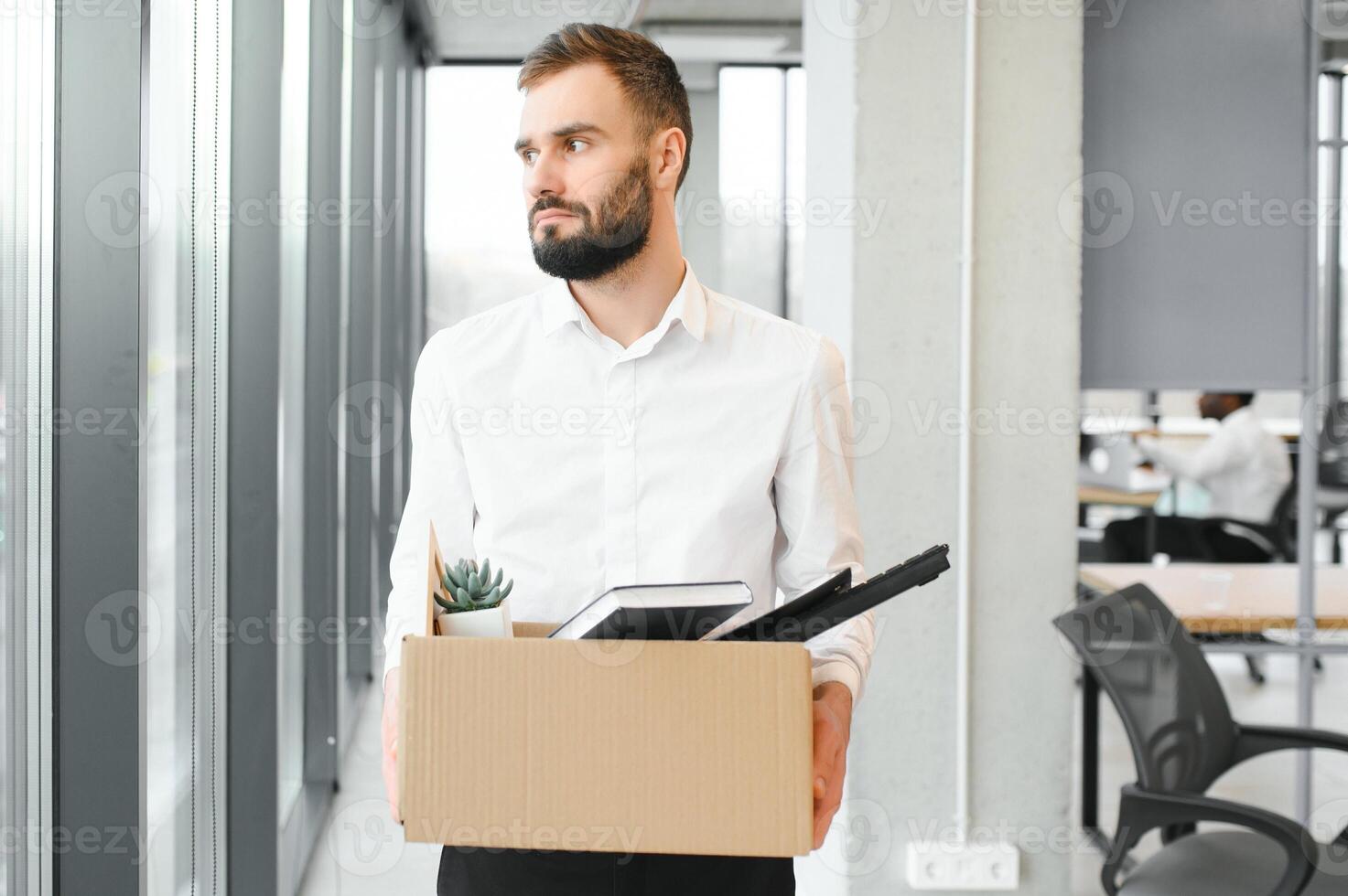 Young handsome businessman in light modern office with carton box. Last day at work. Upset office worker is fired photo