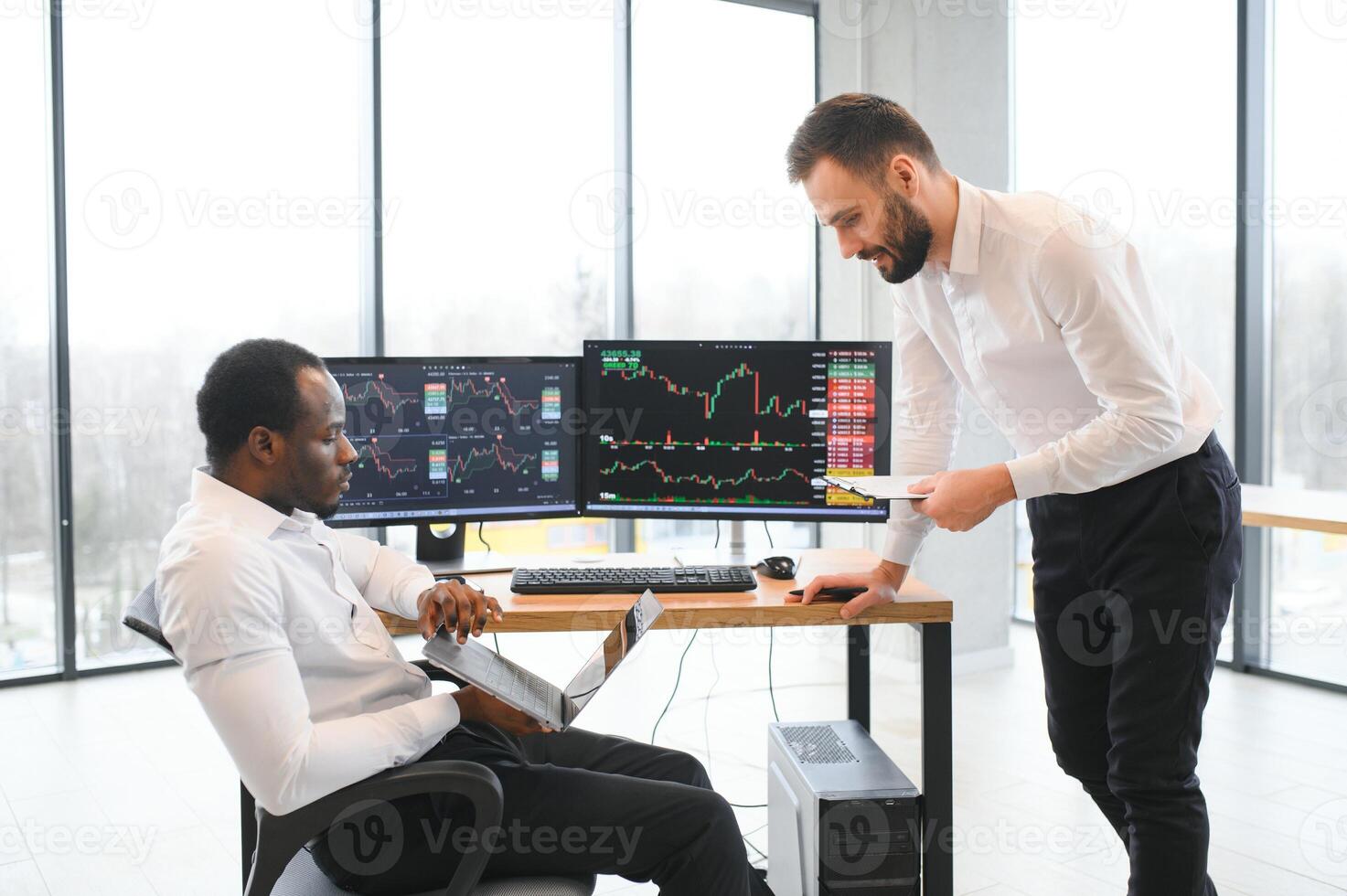 Two successful trader sitting in office, checking cryptocurrency information data on finance market graph, pointing on monitor photo