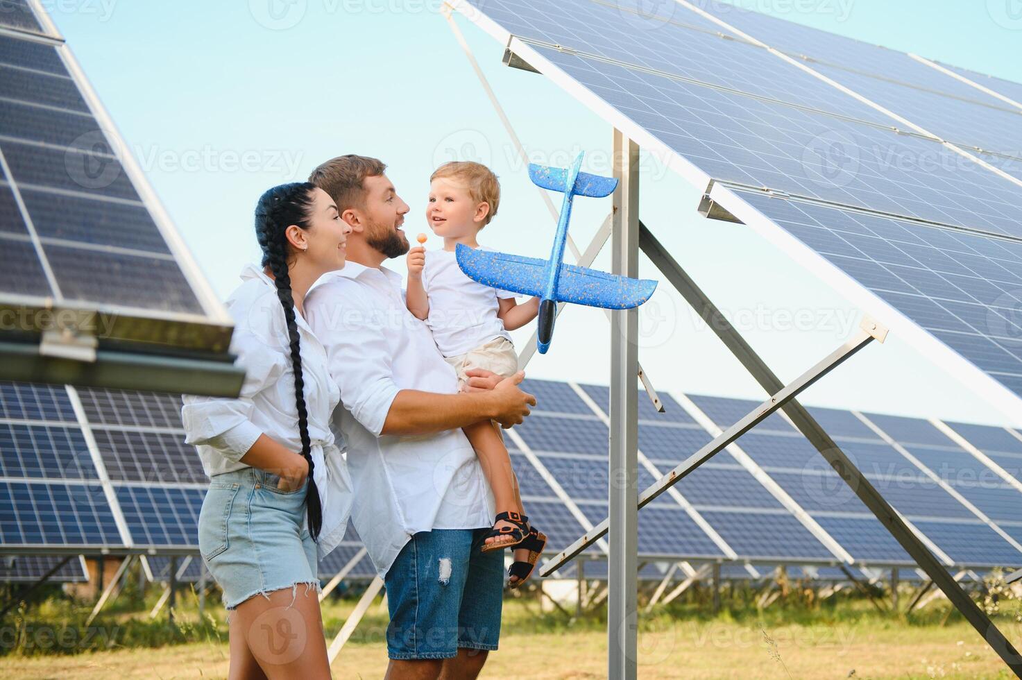 A wide shot of a happy family standing together and smiling at camera with a large solar panel in background photo