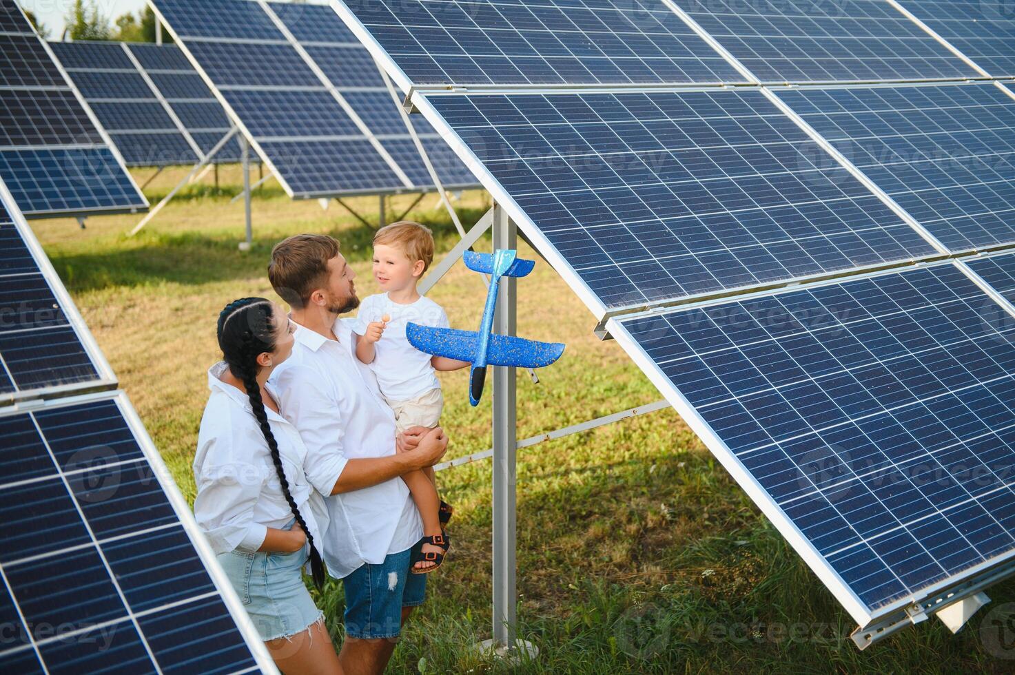Young family with a small child in her arms on a background of solar panels. A man and a woman look at each other with love. Solar energy concept. photo
