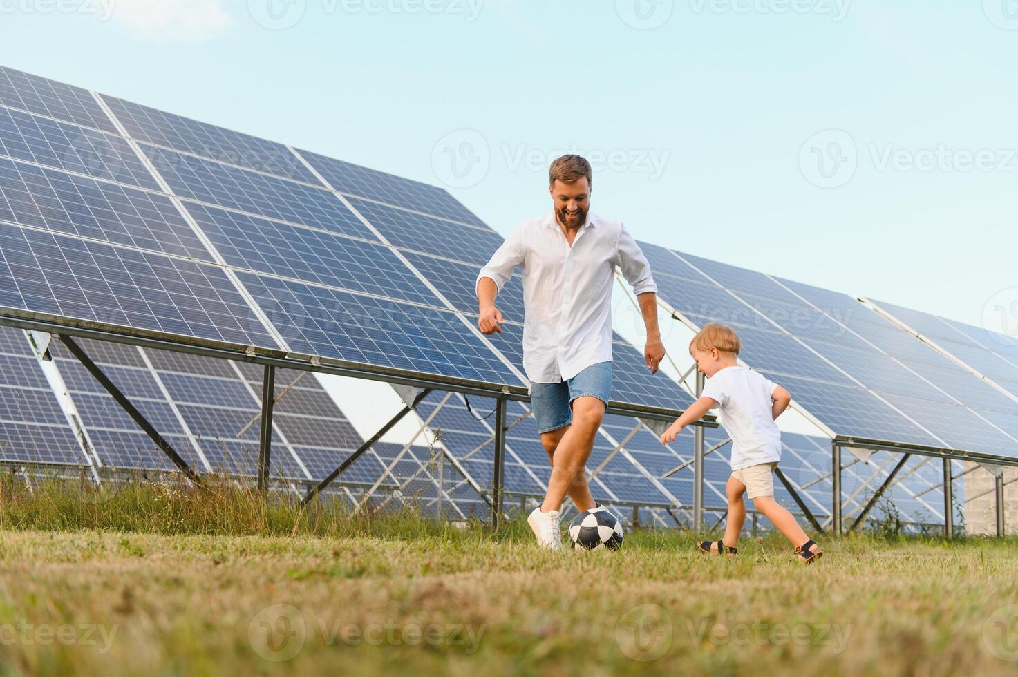 Father and son have fun playing football near the solar panels. The concept of green energy photo