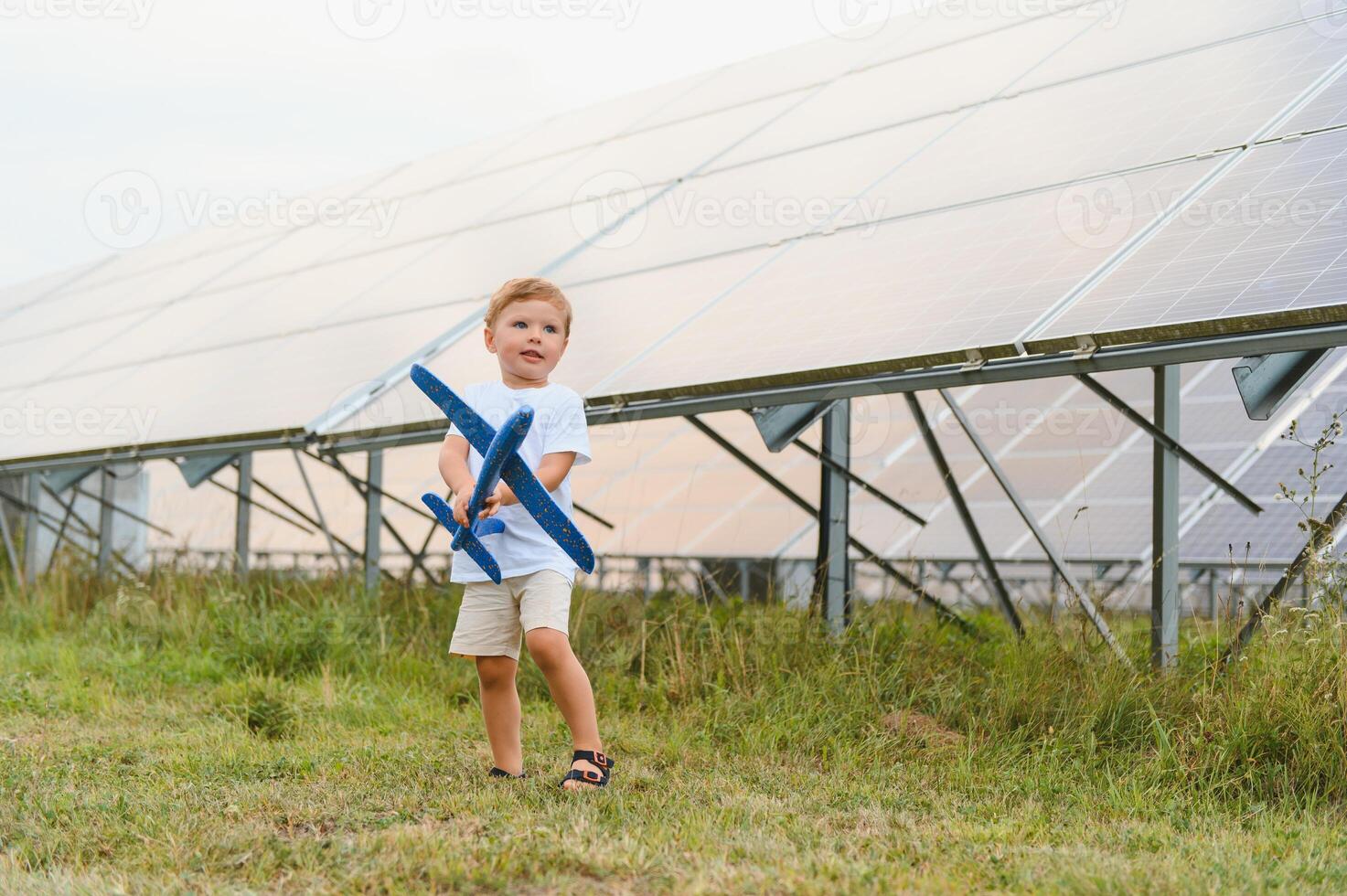 Little happy boy playing with toy airplane near solar panels. photo