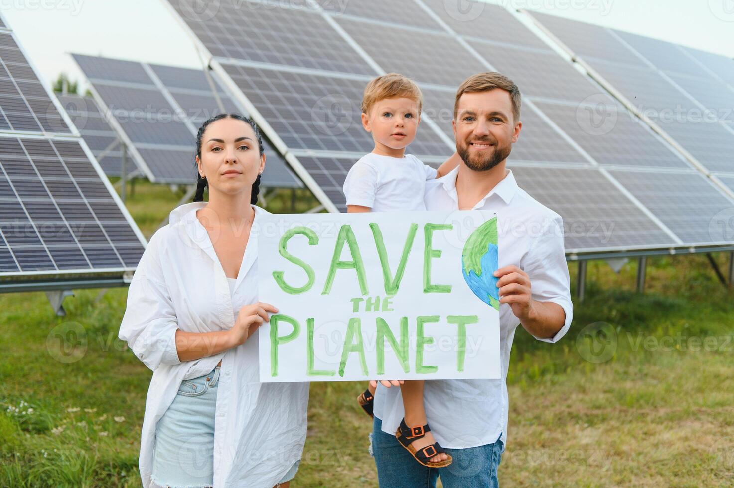 A family of activists and nature defenders stands with a poster about the protection of nature against the background of solar panels. The concept of green energy and nature protection. photo