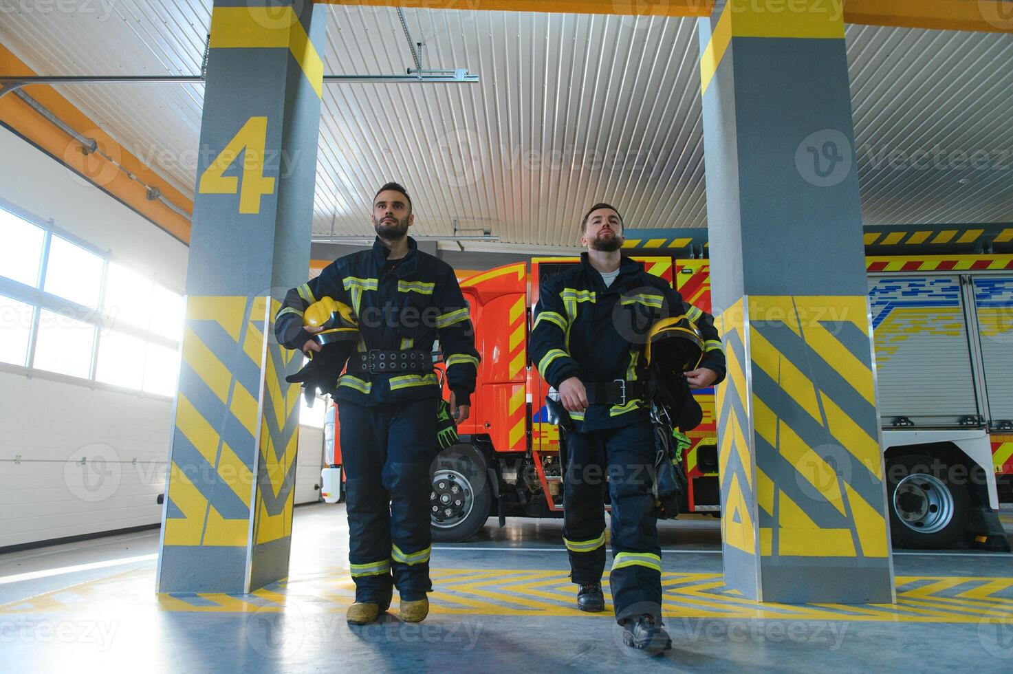 Portrait of two young firemen in uniform standing inside the fire station photo