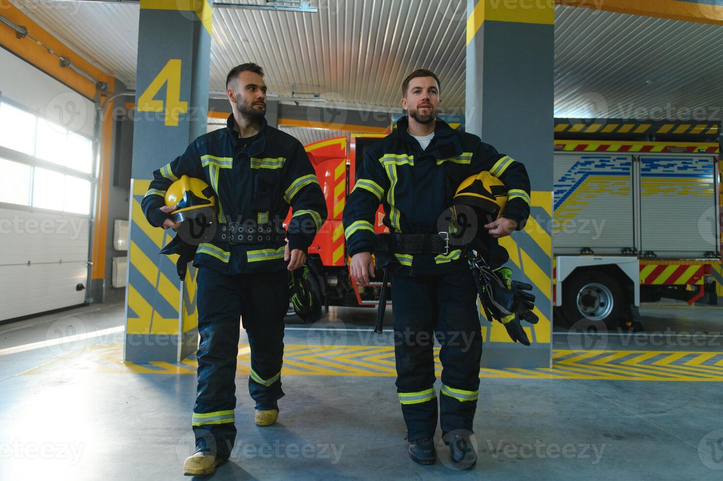 Portrait of two young firemen in uniform standing inside the fire station photo