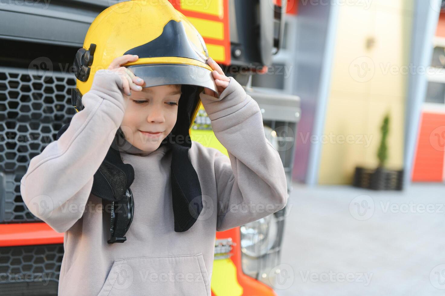 Child, cute boy, dressed in fire fighers cloths in a fire station with fire truck, childs dream photo