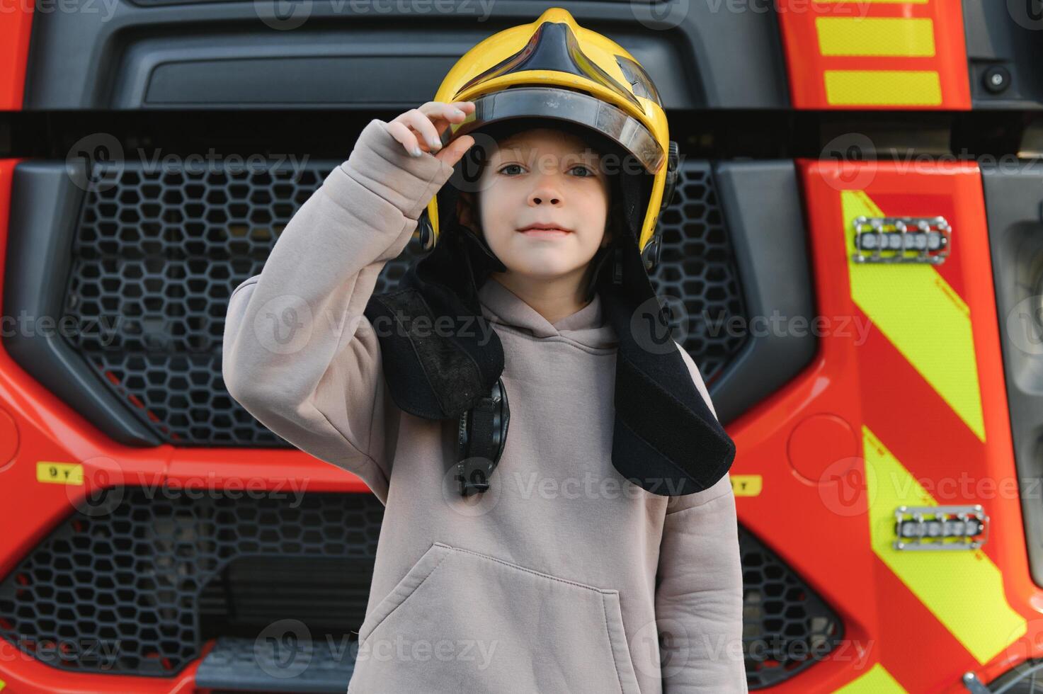 A boy wearing a fireman's helmet near a fire truck. photo