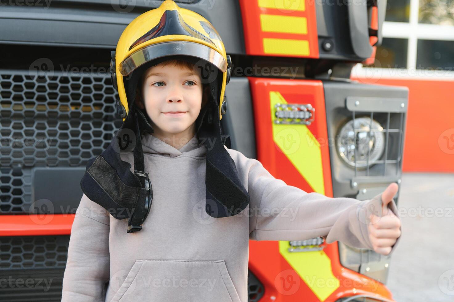 A boy wearing a fireman's helmet near a fire truck. photo