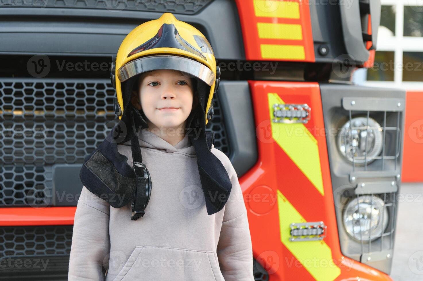 Child, cute boy, dressed in fire fighers cloths in a fire station with fire truck, childs dream photo