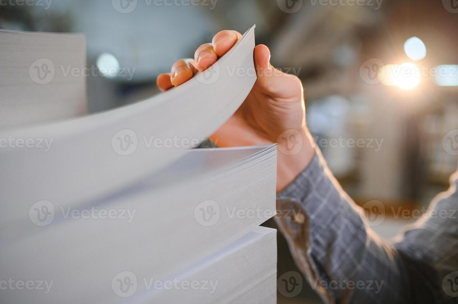 Close up of man putting stack of paper in printing machine at publishing shop, copy space photo