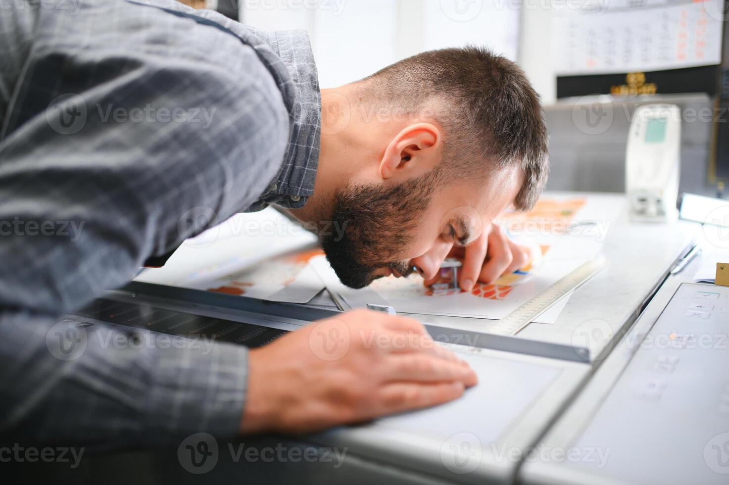 Printing house interior with modern offset print machine and operator in working uniform checking quality and controlling process of print photo