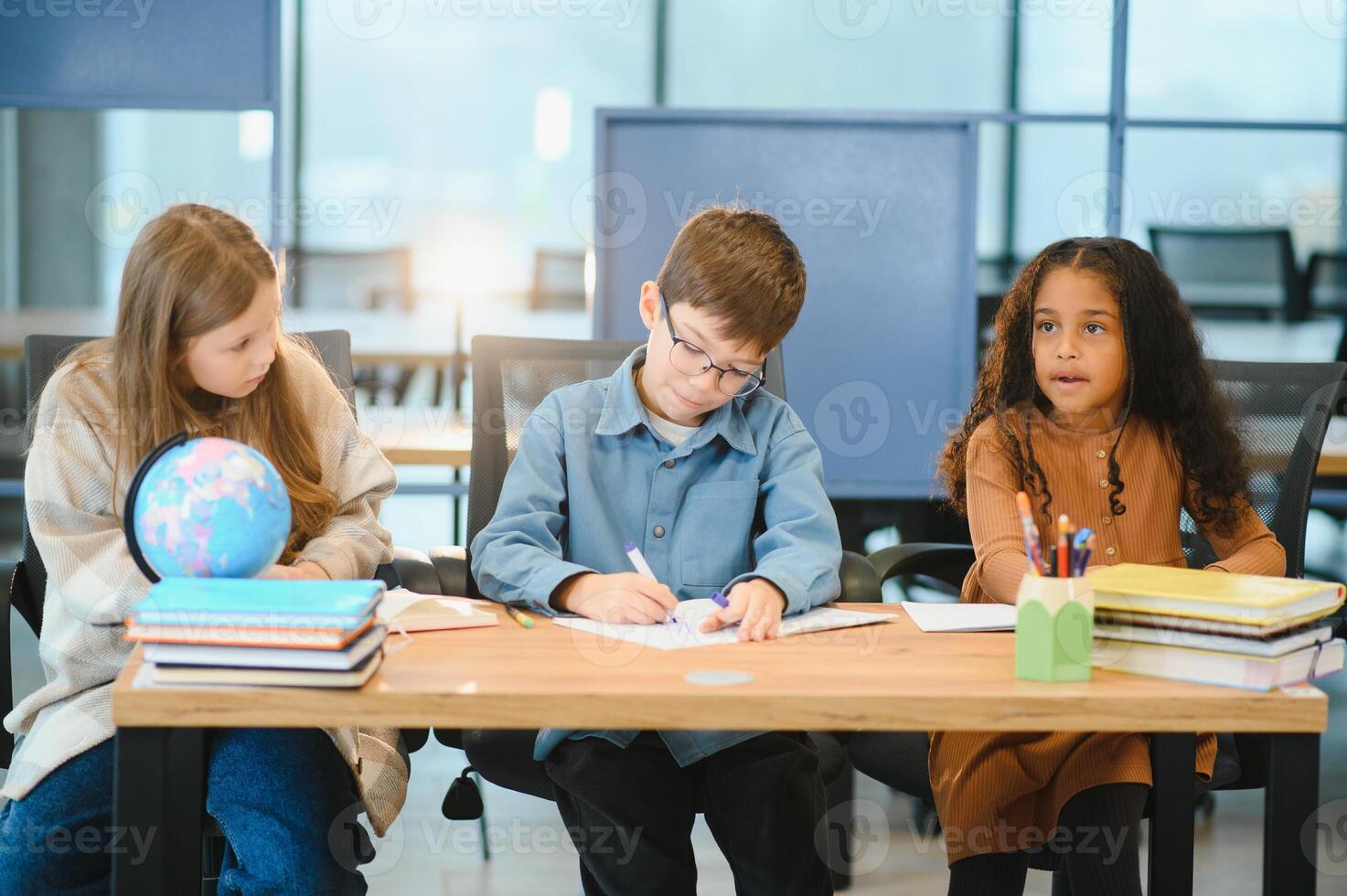 Focused multiracial students kids writing down data into notebook while sitting at table photo