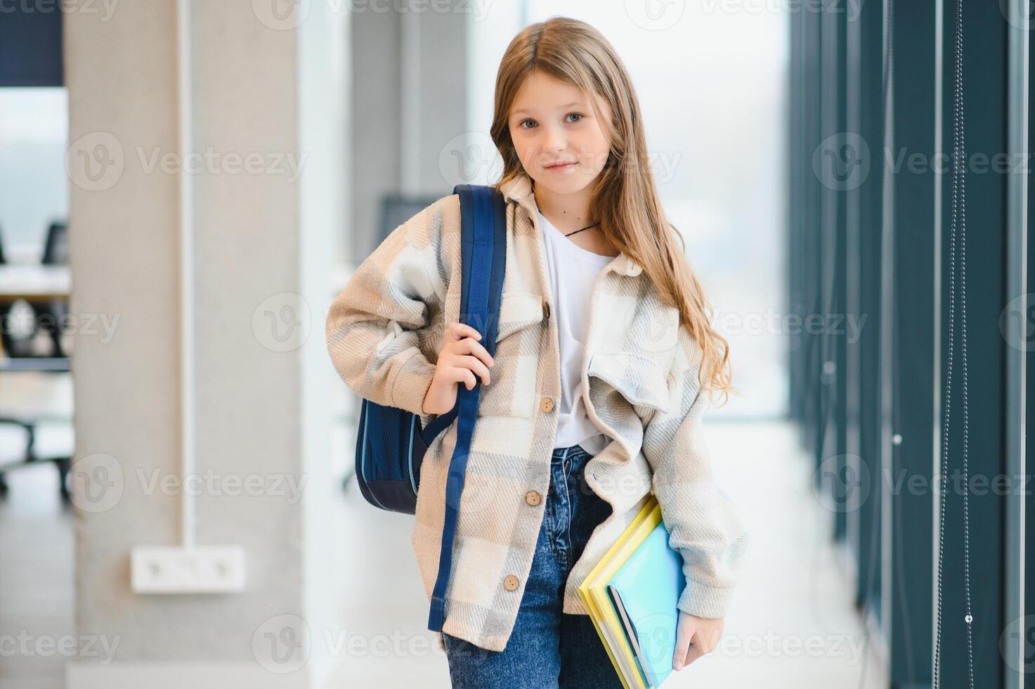 Pretty blonde school girl holding many colorful notes and books. Clever teen girl smiling at camera, standing on corridor of international school photo