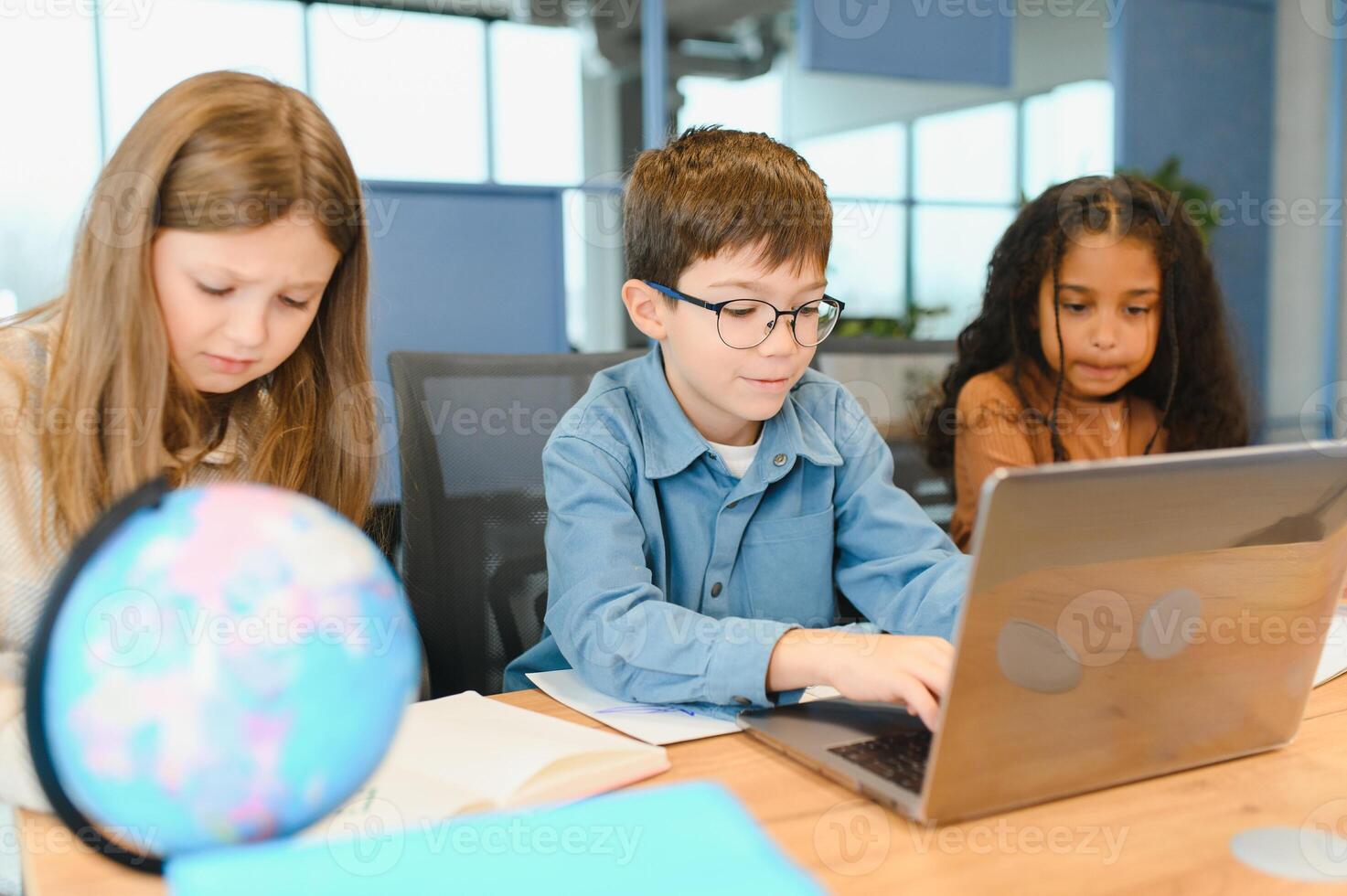 Portrait of smart schoolgirls and schoolboys looking at the laptop in classroom photo