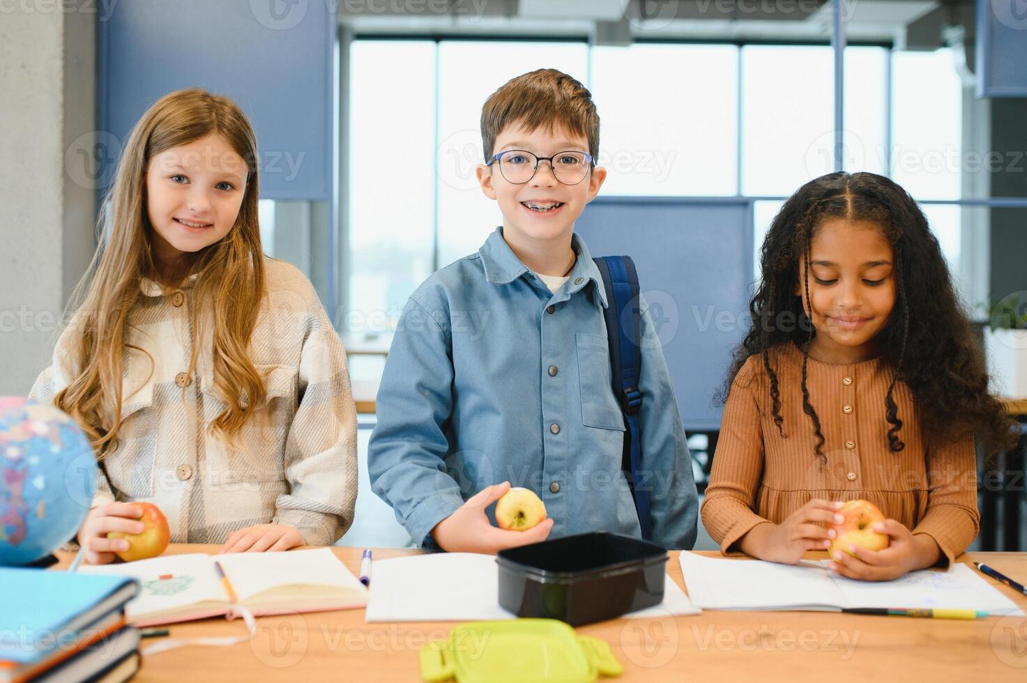 multirracial Niños de escuela teniendo almuerzo a el escritorio durante un descanso en colegio foto