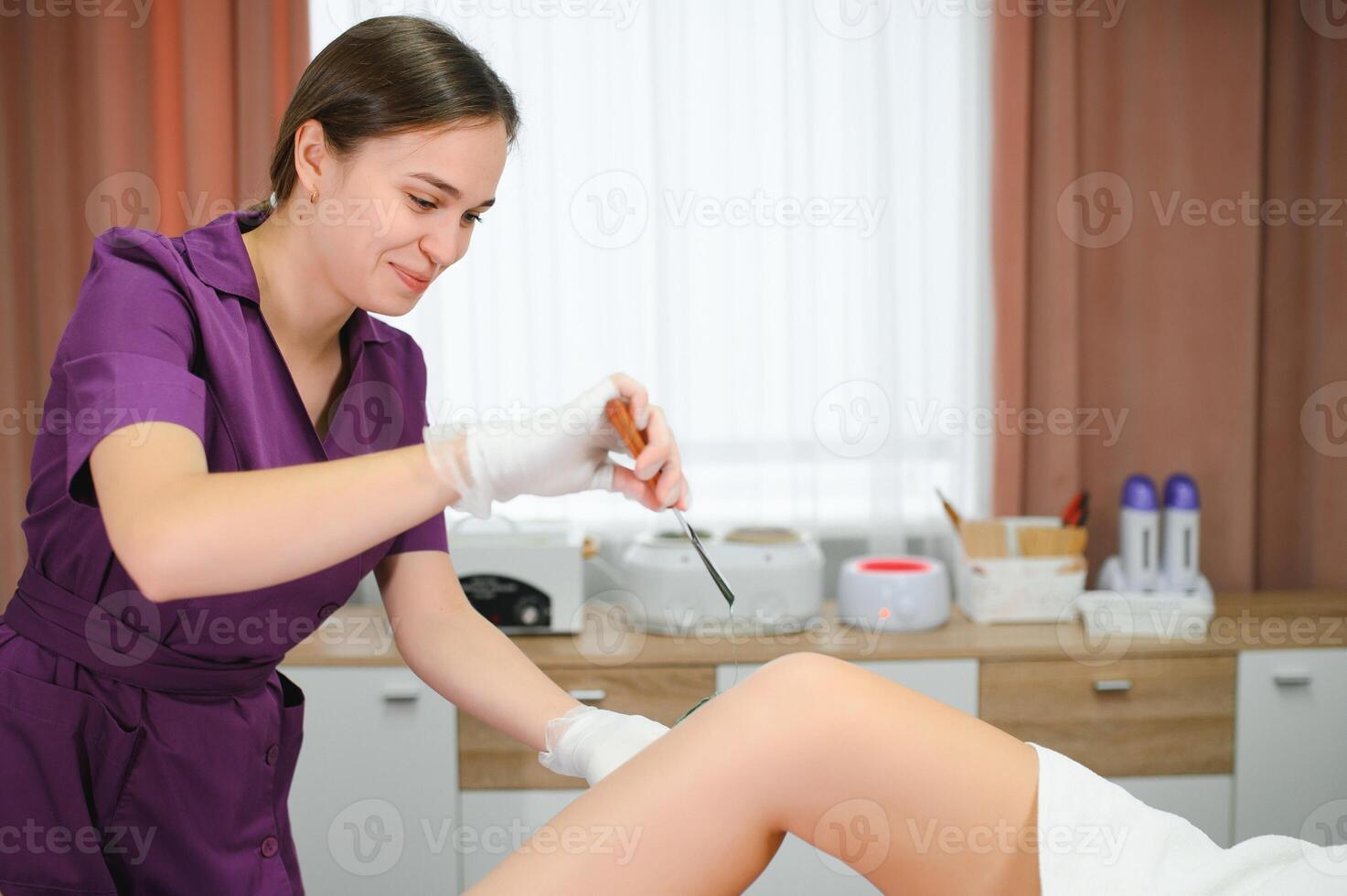 A master applies depilatory wax to a young woman's leg for hair removal. Depilation with wax. Beauty concept. Place for text. Selective focus photo