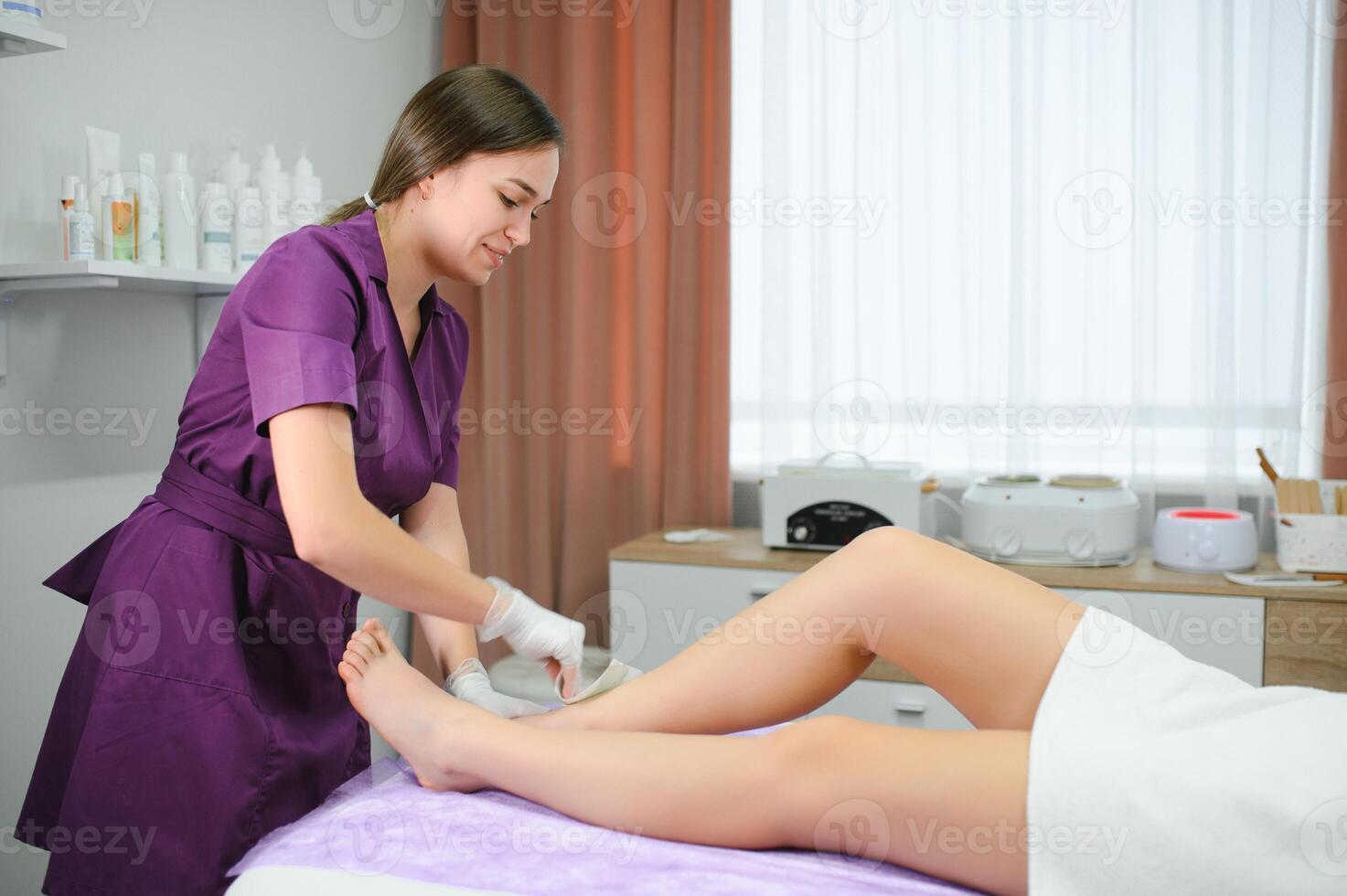 Beautician waxing woman legs in a spa salon photo